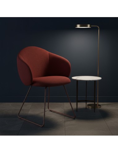 Fauteuil Volta tapissé en bordeaux profond, mis en valeur dans un espace sombre et raffiné avec lampe sur pied et table d’appoin